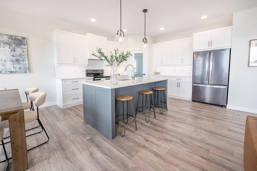 Kitchen with white cabinets, grey island, pendant lights and light brown wood-pattern laminate